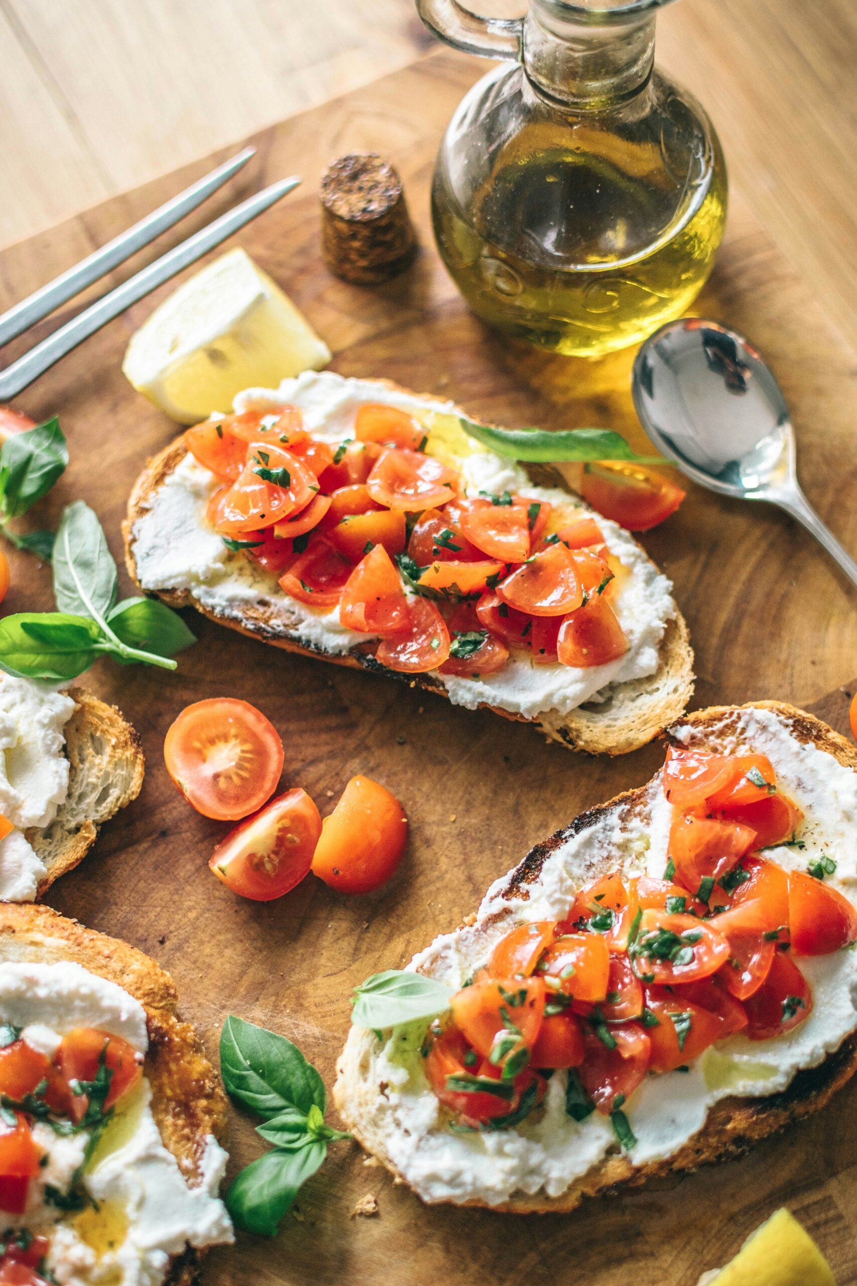 Fresh bruschetta topped with diced tomatoes and basil, served on toasted bread. A bottle of olive oil and lemon wedges are placed alongside, enhancing the Mediterranean presentation. Ideal for a healthy appetizer or snack.